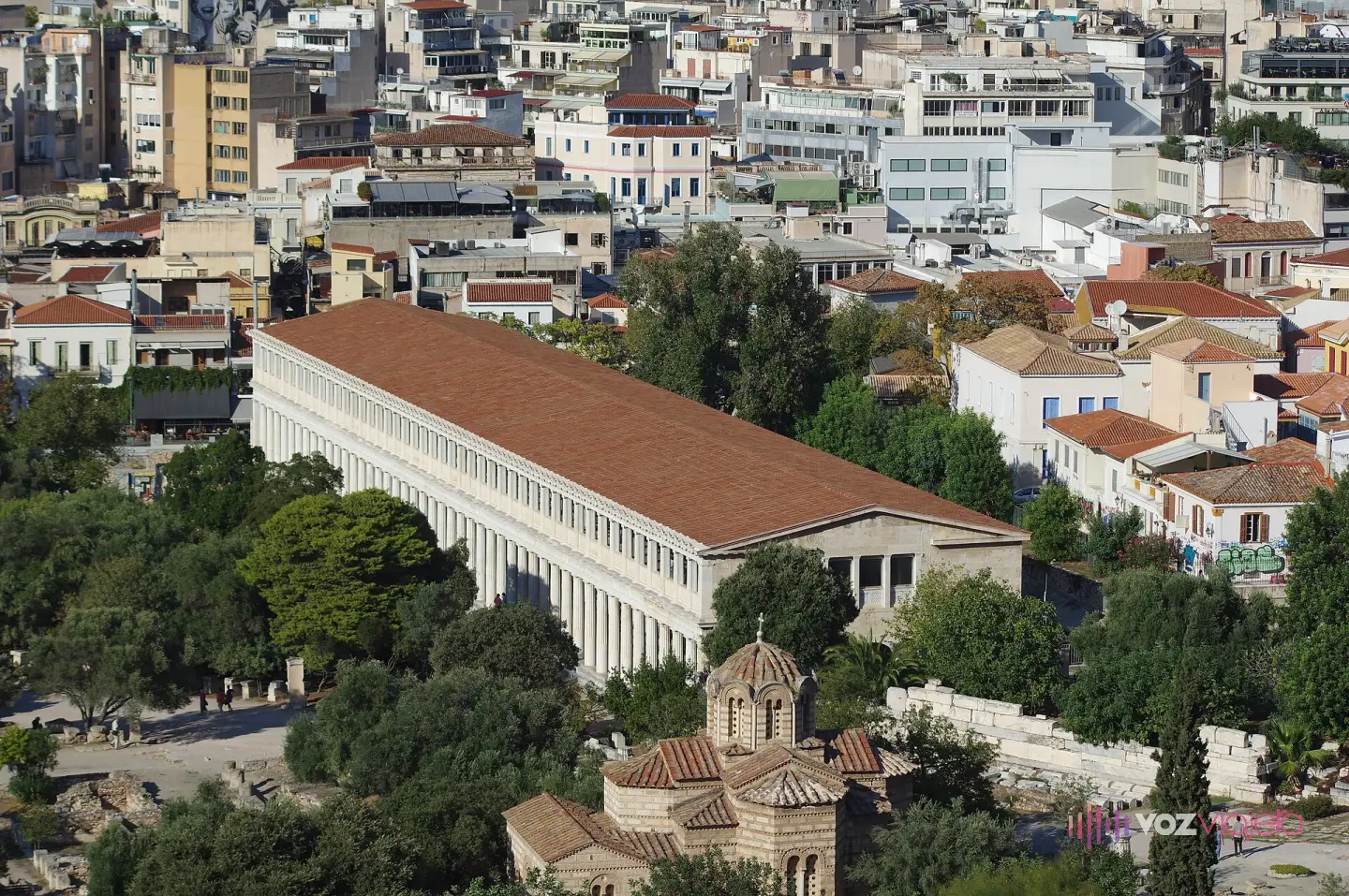 La Estoa de Átalo reconstruida, con sus 2 plantas de columnata blanca y el tejado de tejas rojas, vista desde lo alto; delante, la cúpula de la iglesia de los Santos Apóstoles
