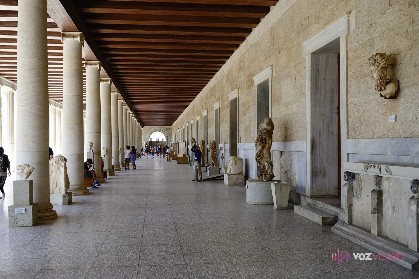 La galería baja de la Estoa de Átalo convertida en museo, con estatuas y relieves alineados entre las columnas y el techo de vigas de madera al fondo