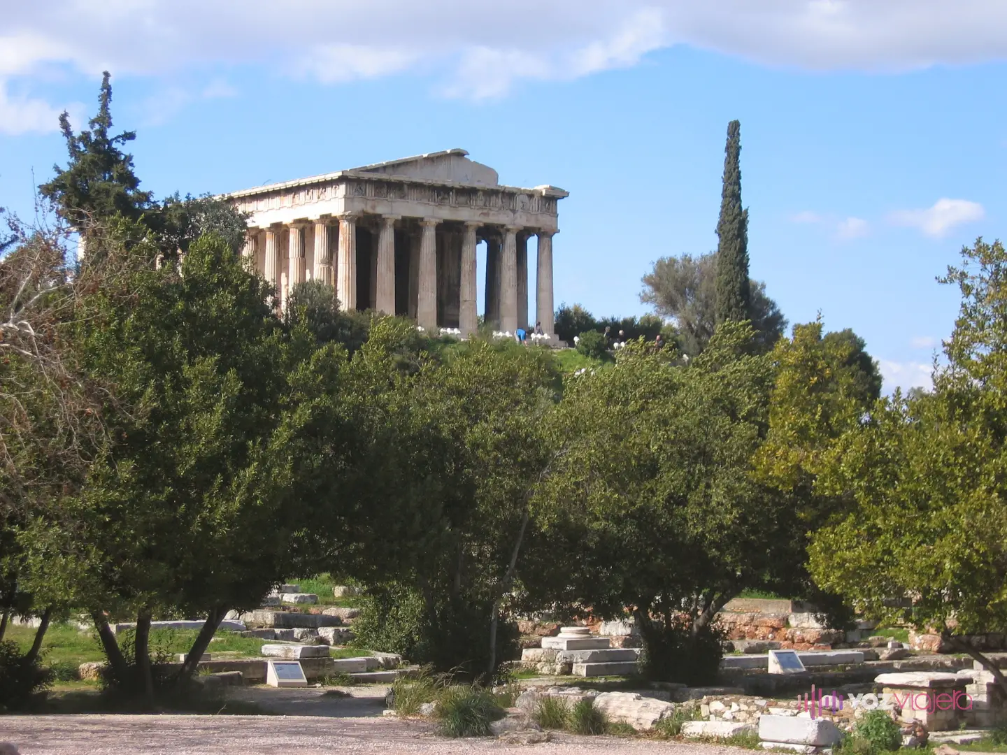 El recinto del Ágora de Atenas visto desde abajo, con los cimientos y los bloques de los edificios antiguos entre olivos y, en lo alto de la colina, el Templo de Hefesto entero