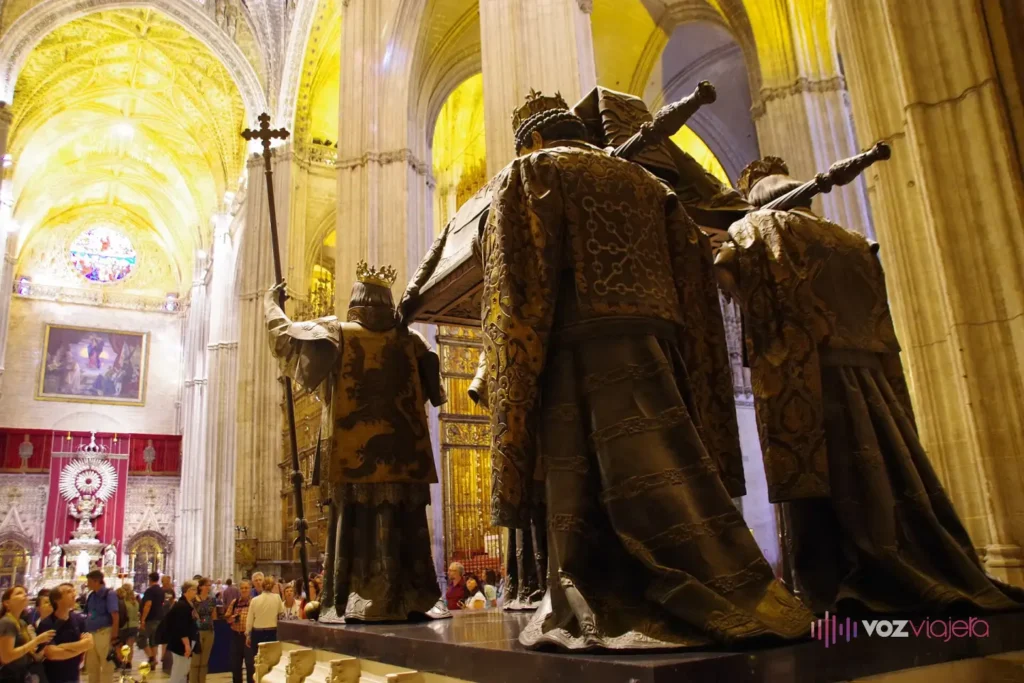 Sepulcro de Cristóbal Colón en la Catedral de Sevilla: cuatro heraldos de bronce llevan el féretro a hombros, con visitantes alrededor