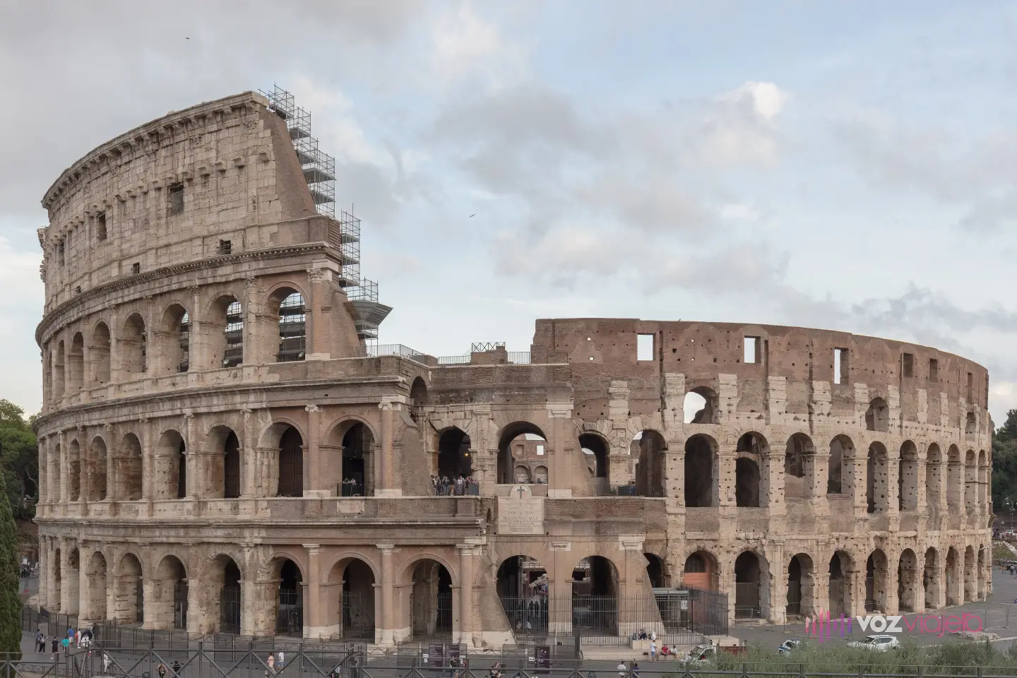 Fachada exterior del Coliseo de Roma con sus 4 pisos: 3 órdenes de arcos superpuestos y un ático con ventanas; a la izquierda se conserva la altura completa del anillo exterior, con andamios en lo alto, y a la derecha asoma el anillo interior, más bajo