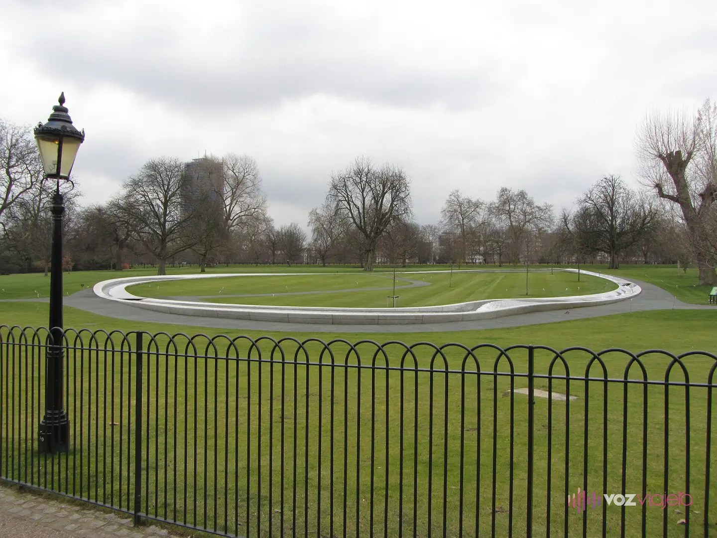 La fuente en memoria de Diana de Gales en Hyde Park: un anillo ovalado de granito claro sobre el césped, rodeado por una verja baja y una farola