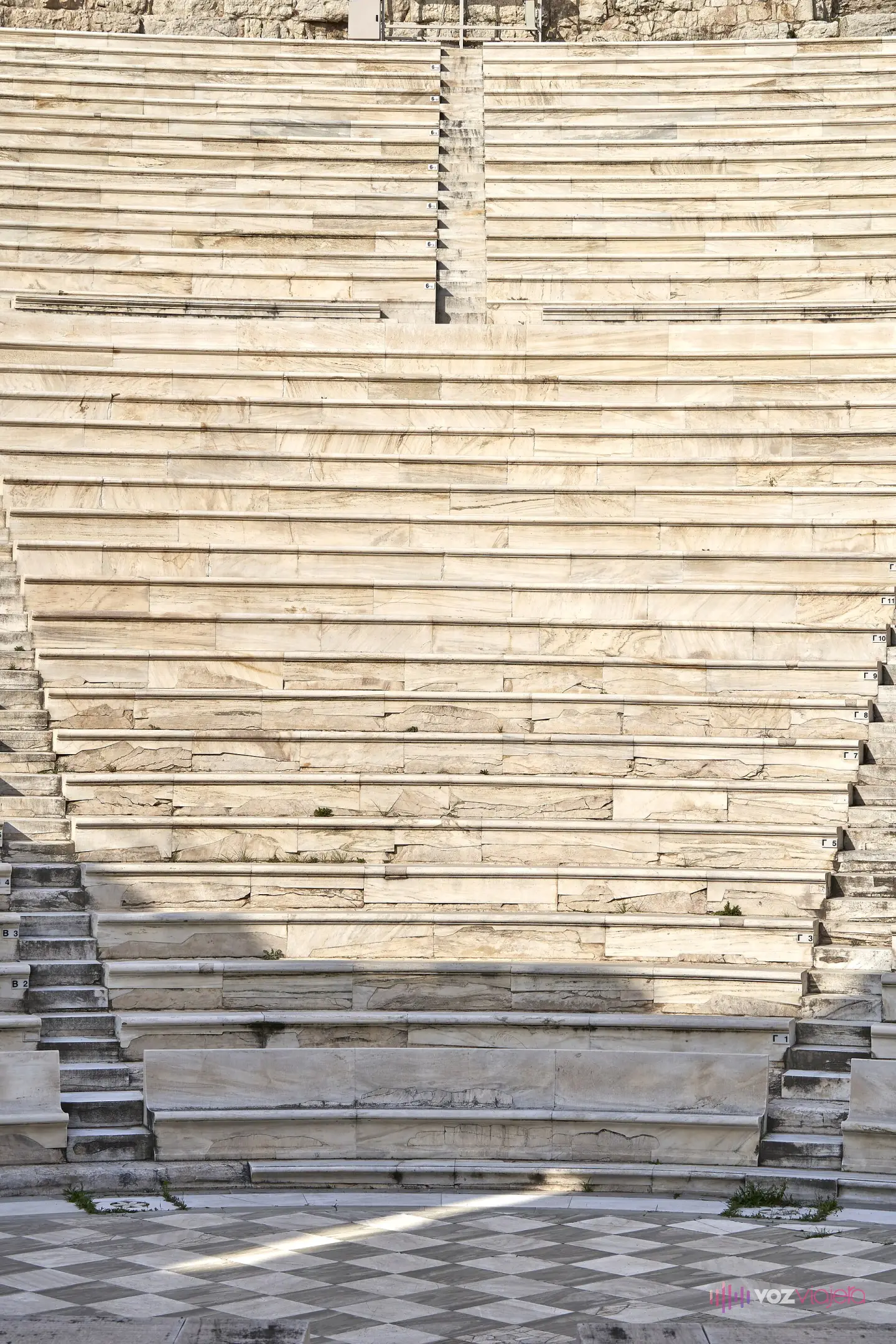 Las filas de mármol restauradas de un kerkis, con la numeración de asiento fila por fila, bajando hasta el pavimento ajedrezado de la orquestra