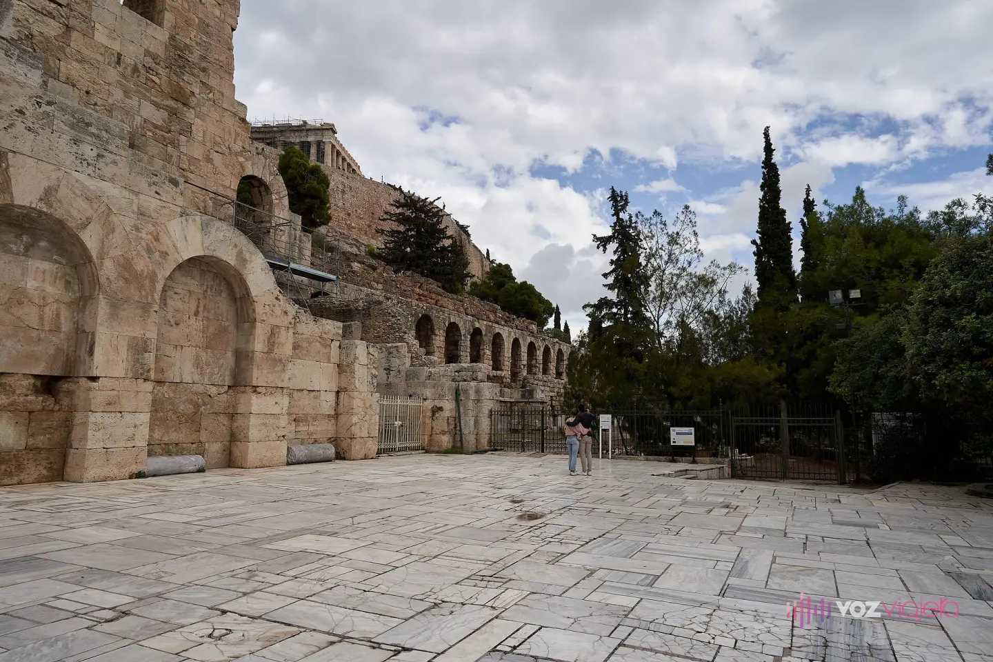 El Odeón al pie de la Acrópolis desde la explanada de la ladera sur, con los arcos de la Estoa de Eumenes prolongando el muro hacia el este y el Partenón asomando arriba