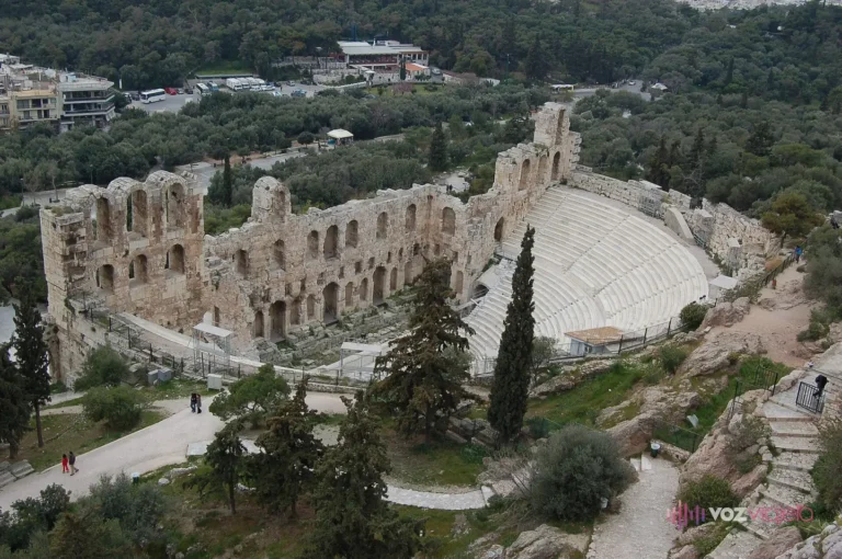 Planta completa del Odeón desde lo alto de la Acrópolis: el graderío de mármol blanco en semicírculo, encajado en la ladera y cerrado por delante por el muro de escena de dos pisos de arcos