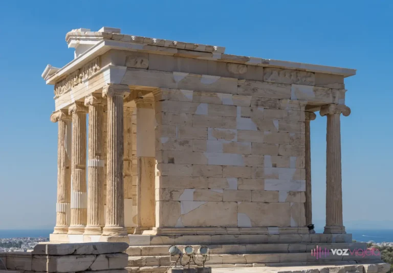 El Templo de Atenea Niké entero, visto desde una esquina: las 4 columnas jónicas de un extremo, el muro liso de la cela sin ninguna columna en el flanco y las del otro extremo asomando al fondo, con cielo despejado y el mar al horizonte