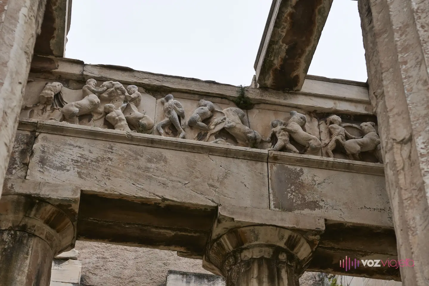 Detalle del friso esculpido del Templo de Hefesto visto desde abajo: figuras humanas desnudas peleando cuerpo a cuerpo con centauros, en alto relieve sobre la banda de mármol, con dos capiteles dóricos debajo
