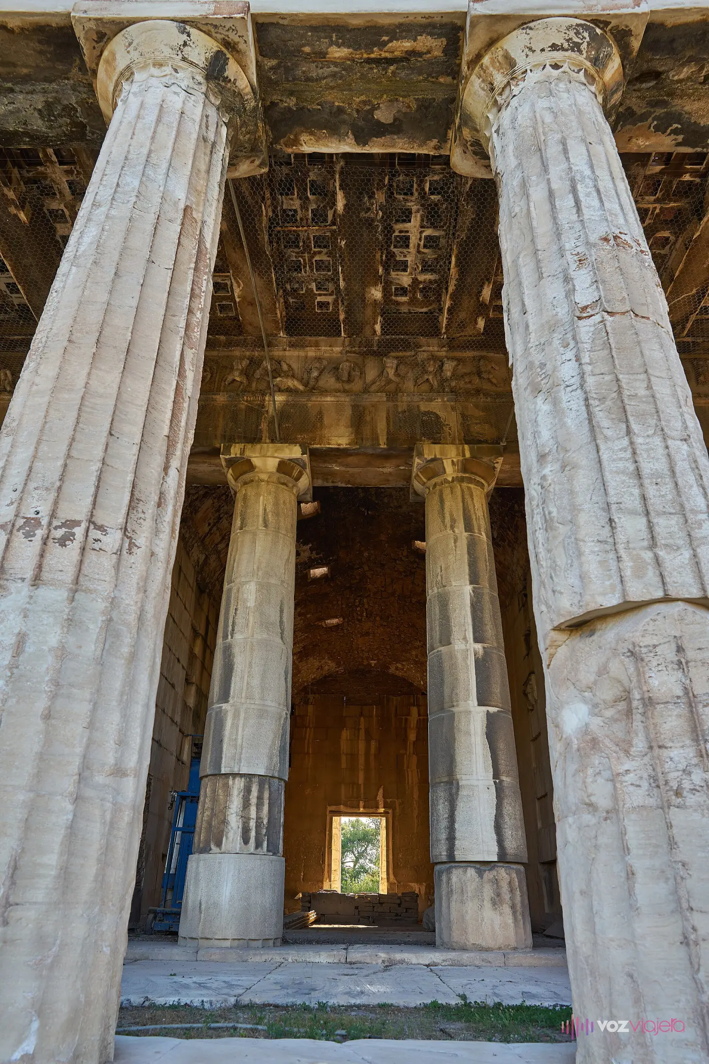 Vista hacia el interior del Templo de Hefesto entre dos columnas del peristilo: el techo de casetones de mármol, el friso esculpido, las dos columnas del pronaos y, al fondo, la cella entera hasta la puerta que se abre al otro extremo