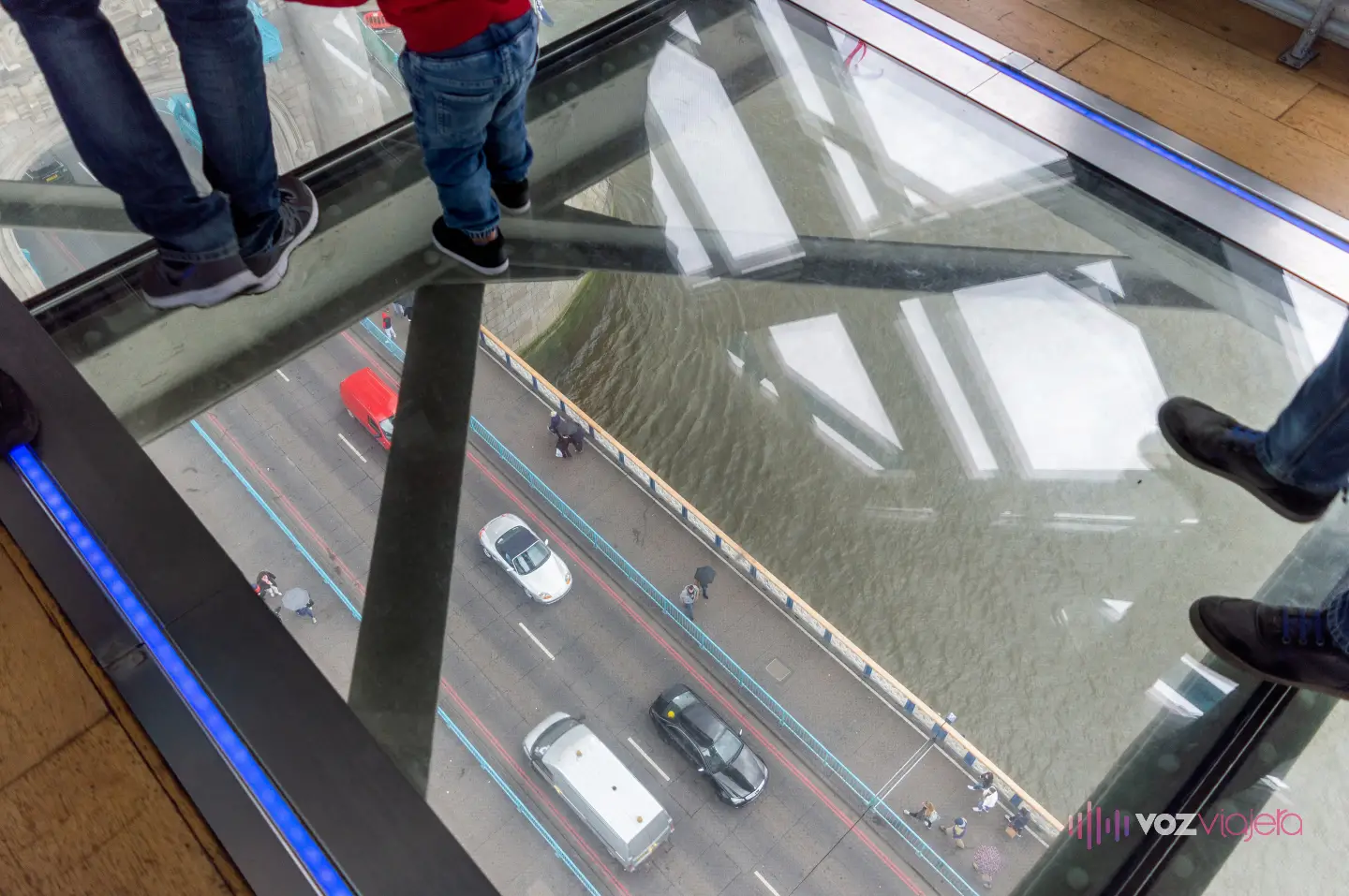 Suelo de cristal de una pasarela alta de Tower Bridge: los pies de los visitantes sobre el vidrio y, muy abajo, la calzada con coches y peatones y el agua del Támesis