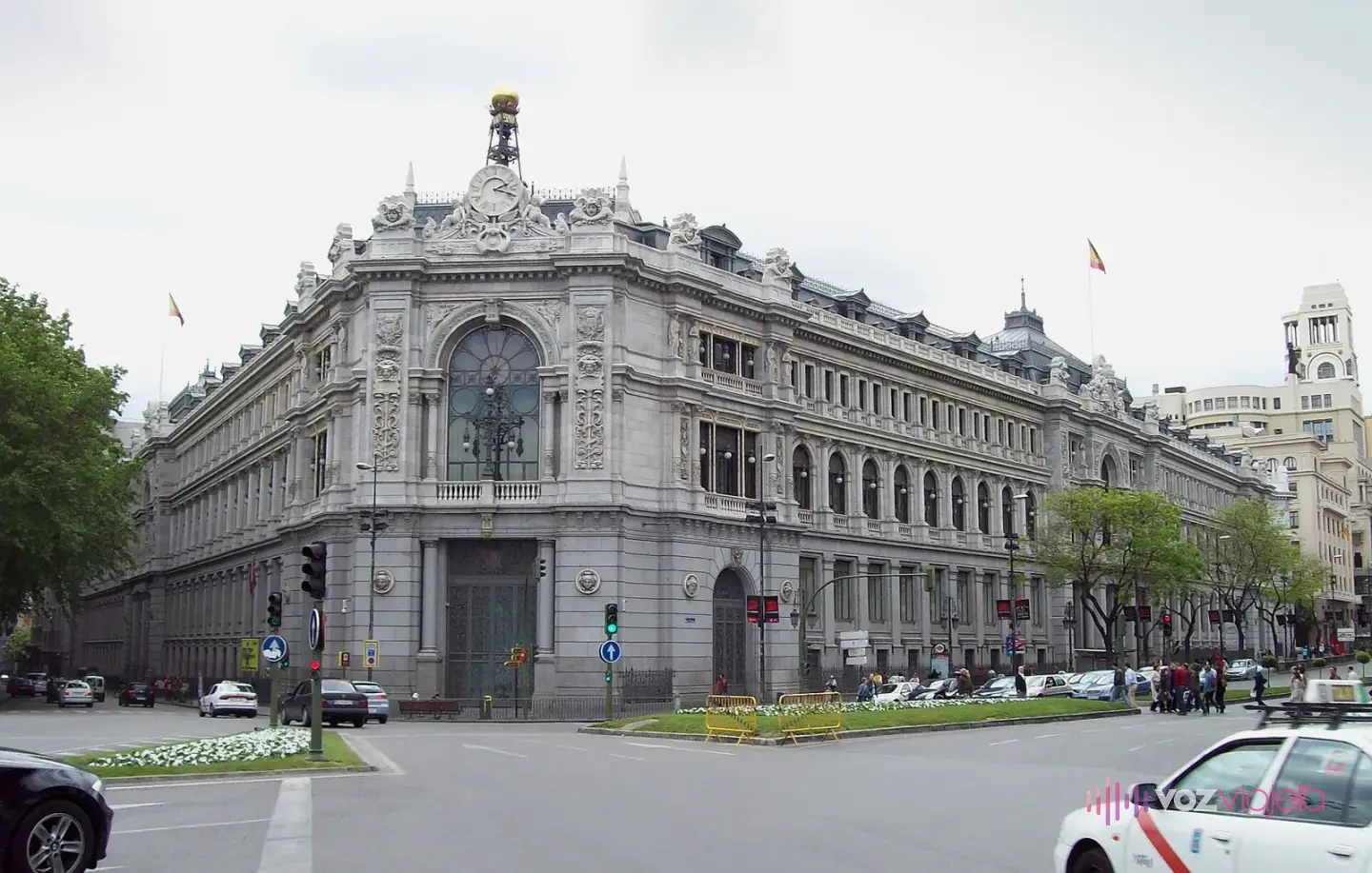 El edificio del Banco de España en la esquina de la Plaza de Cibeles, con su fachada de piedra en chaflán y un gran reloj rematado por una bola dorada sobre la entrada