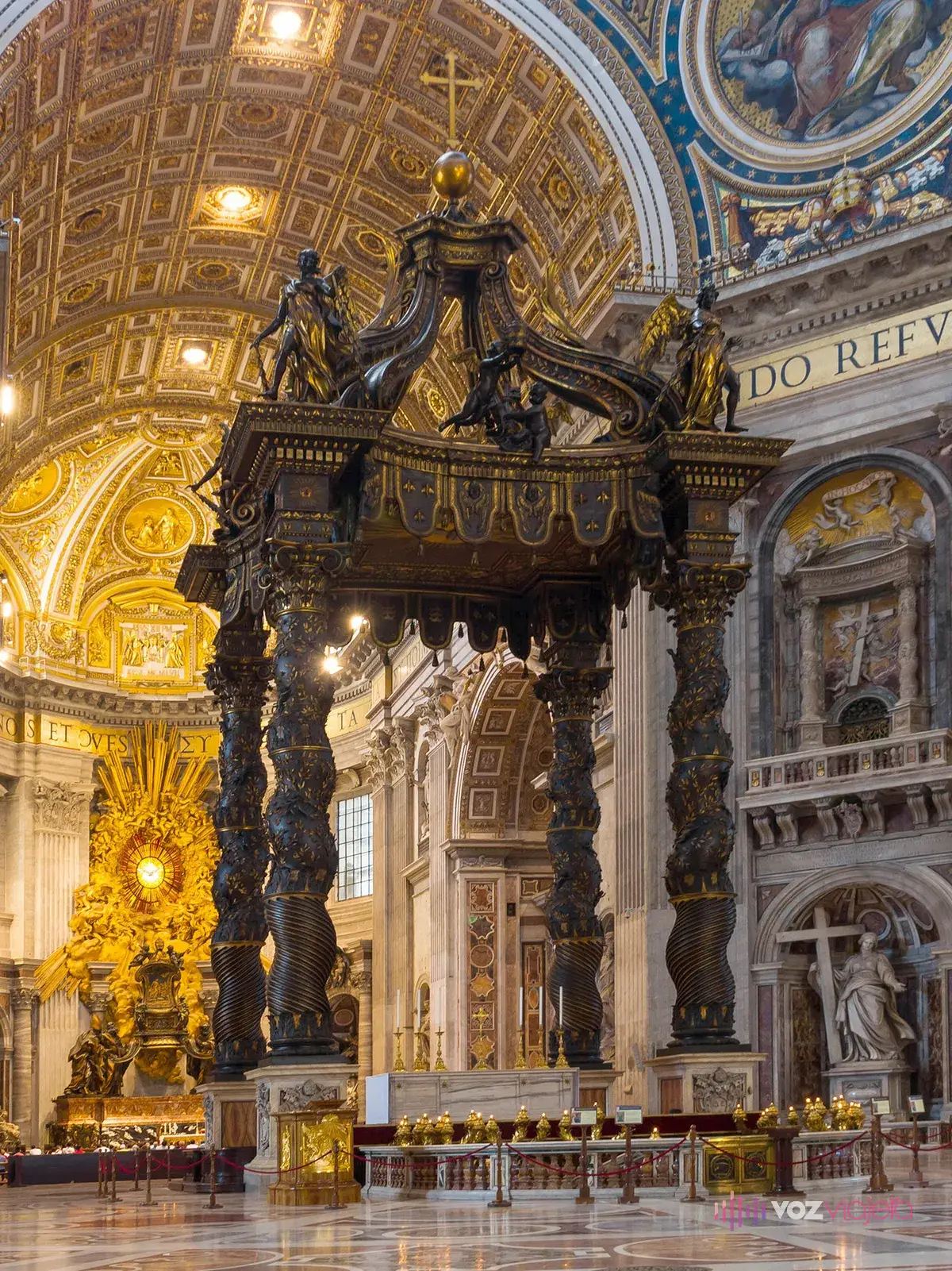 Baldaquino de bronce de Bernini en la Basílica de San Pedro: 4 columnas salomónicas oscuras con un dosel coronado por ángeles y una cruz sobre el altar papal, y al fondo del ábside la Cátedra de San Pedro dorada