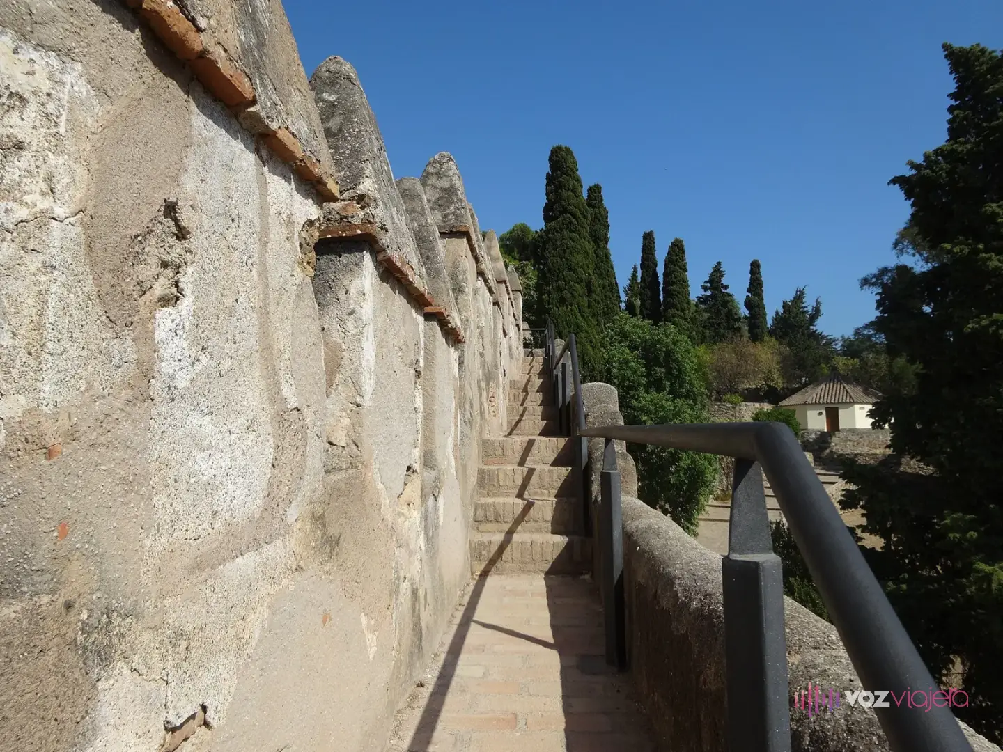 Camino de ronda estrecho con escalones y barandilla metálica junto a las almenas del castillo de Gibralfaro