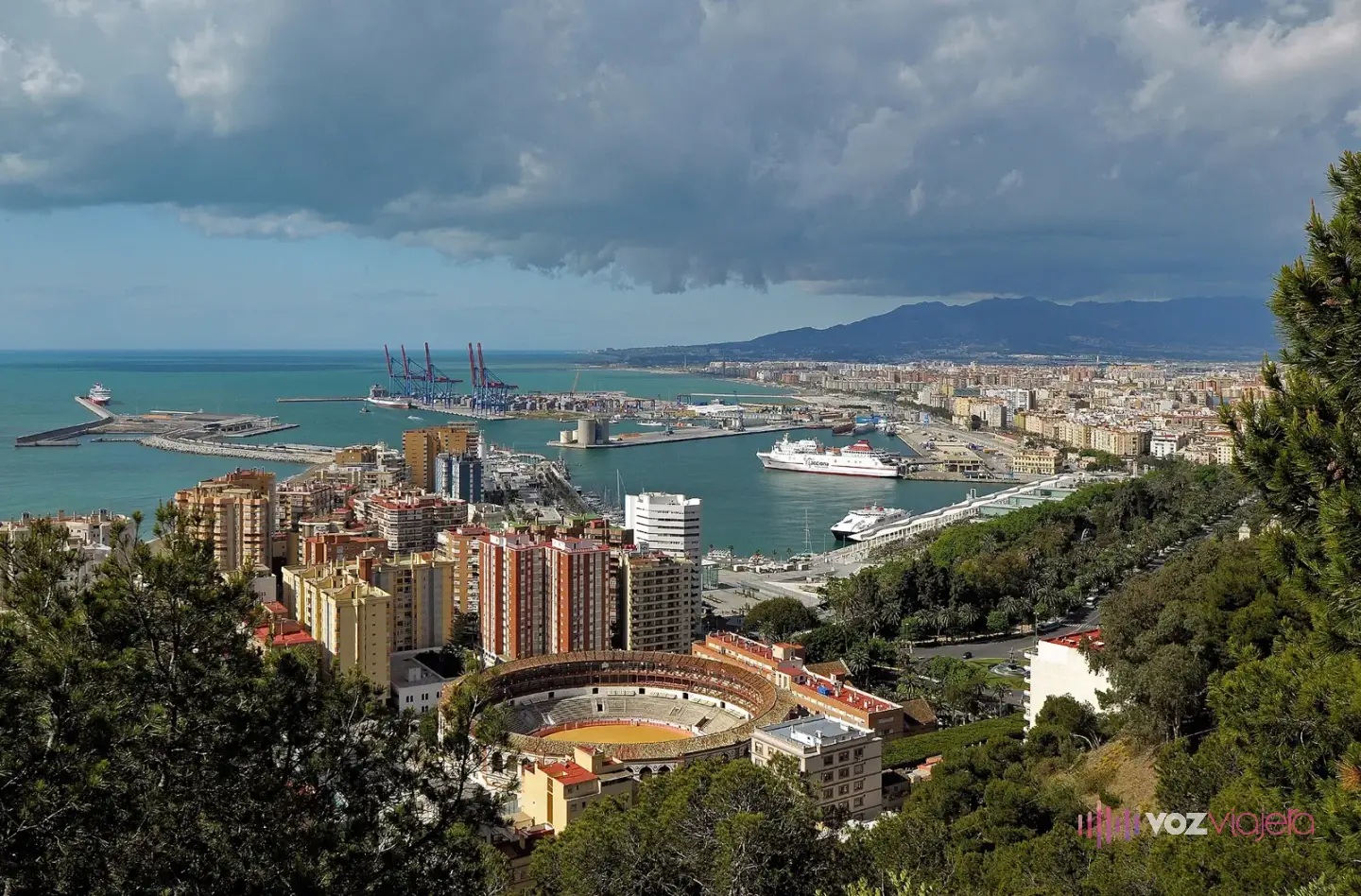 Vista de Málaga desde Gibralfaro: la plaza de toros en primer plano, edificios, el puerto con un ferri y el mar