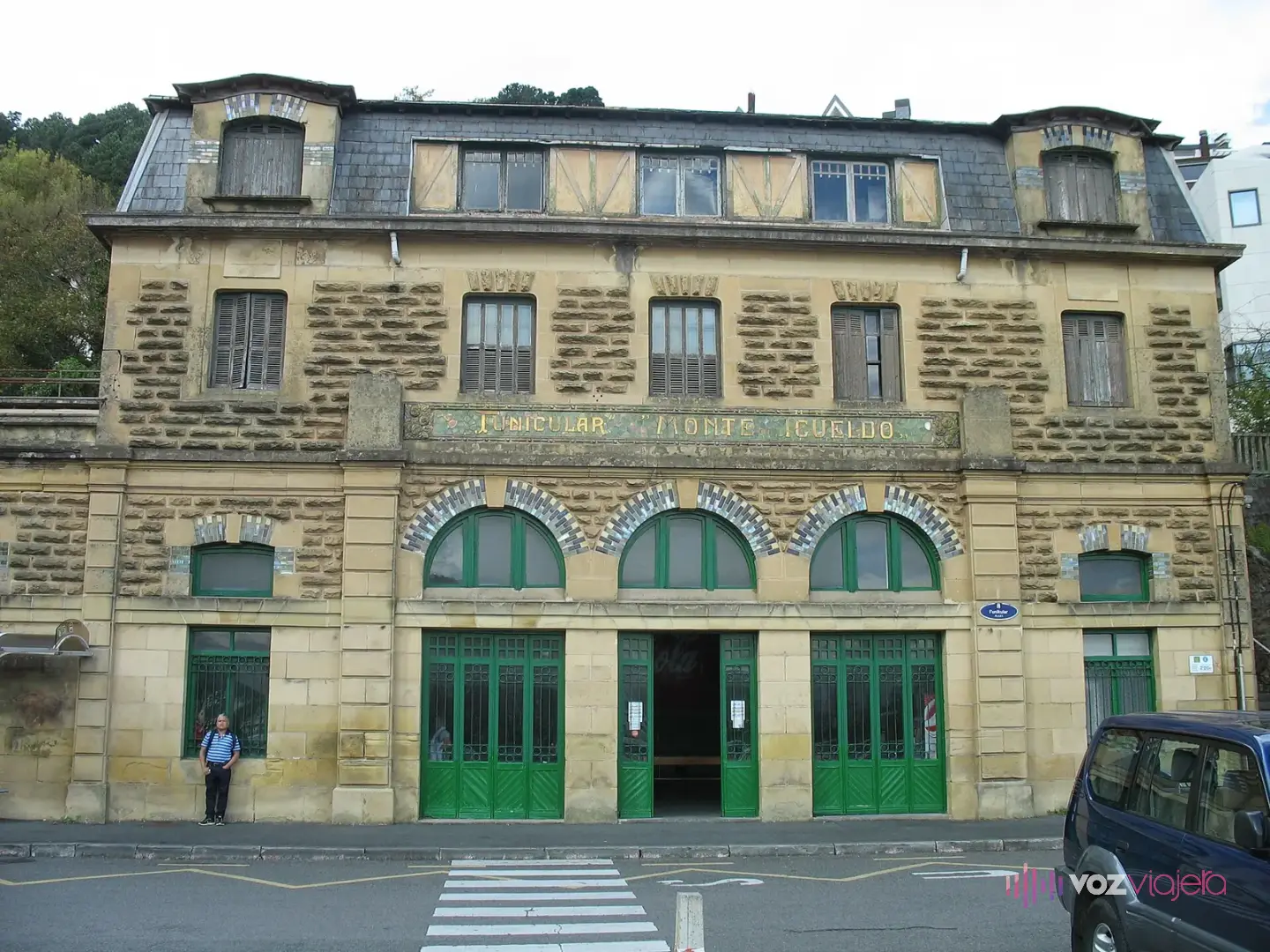 Fachada de piedra de la estación inferior del funicular de Igueldo, con tejado de pizarra, 3 arcos sobre puertas verdes y el rótulo del funicular