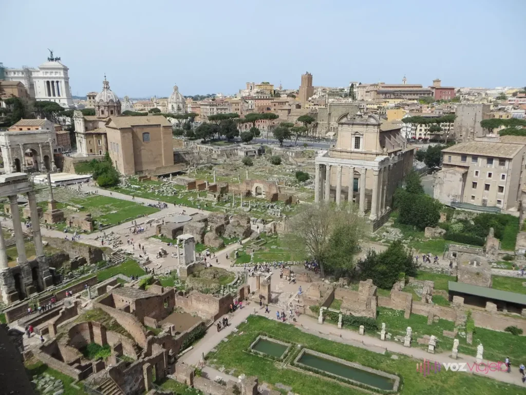 El Foro Romano visto desde el lado del Palatino: en primer plano el largo patio de la Casa de las Vestales con sus estanques y estatuas, a la derecha las columnas del Templo de Antonino y Faustina con una fachada de iglesia detrás, y al fondo la Curia de ladrillo y el Arco de Septimio Severo bajo el Vittoriano blanco