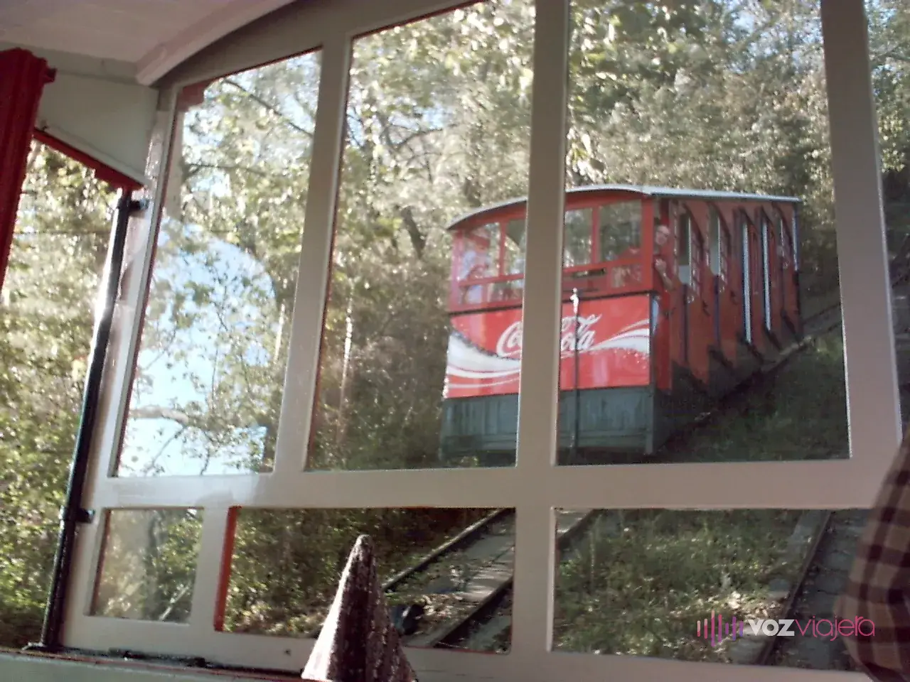 El otro vagón del funicular de Igueldo visto desde la ventana de un vagón, entre árboles, cuando los 2 se cruzan a mitad de la subida