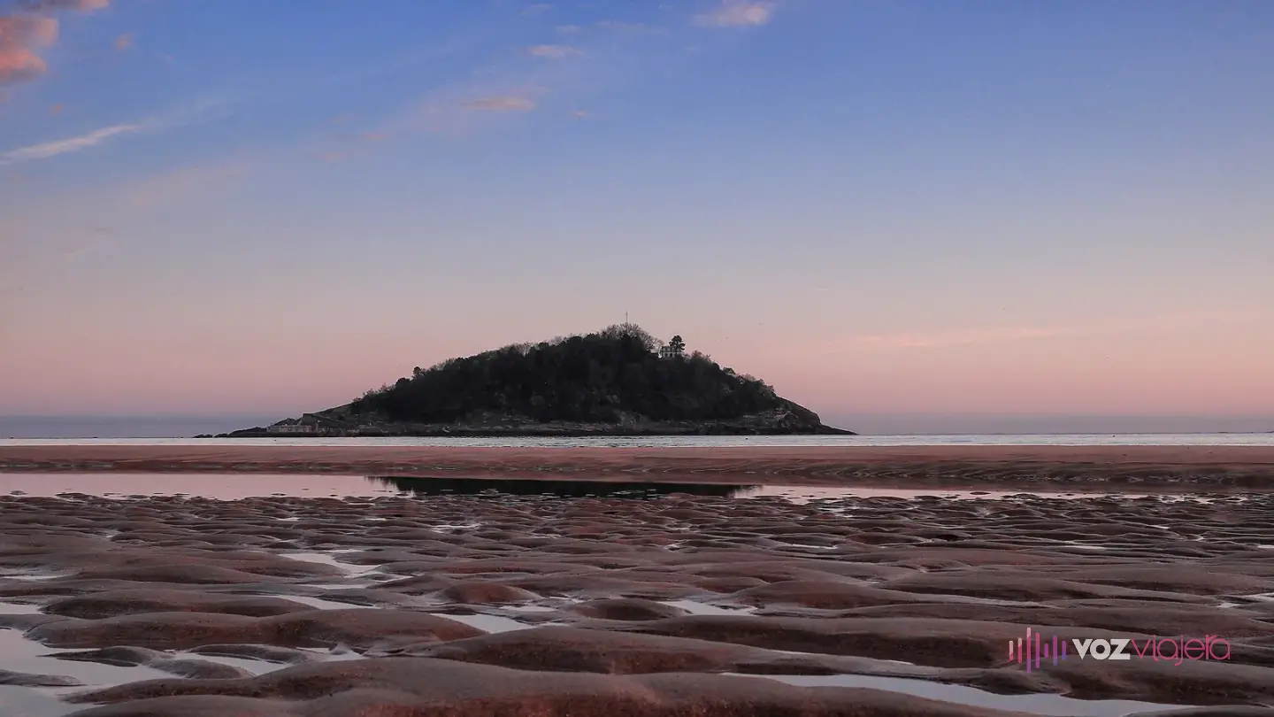 La isla de Santa Clara al amanecer vista desde la playa de La Concha, con la arena mojada y llena de surcos en primer plano