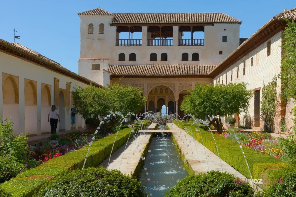 El Patio de la Acequia del Generalife: un canal largo con surtidores entre parterres de flores y setos, cerrado por un pabellón con galería de arcos al fondo