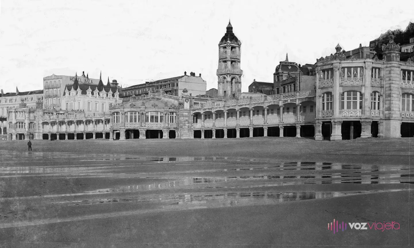 Fotografía antigua en blanco y negro del balneario La Perla del Océano sobre la playa de La Concha, con la arena mojada en primer plano