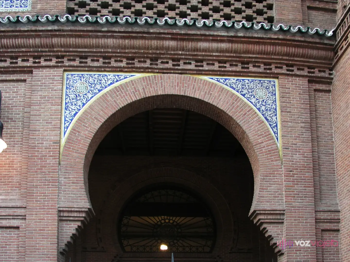 Arco de herradura de ladrillo de Las Ventas enmarcado por azulejos blancos y azules y una celosía de ladrillo encima