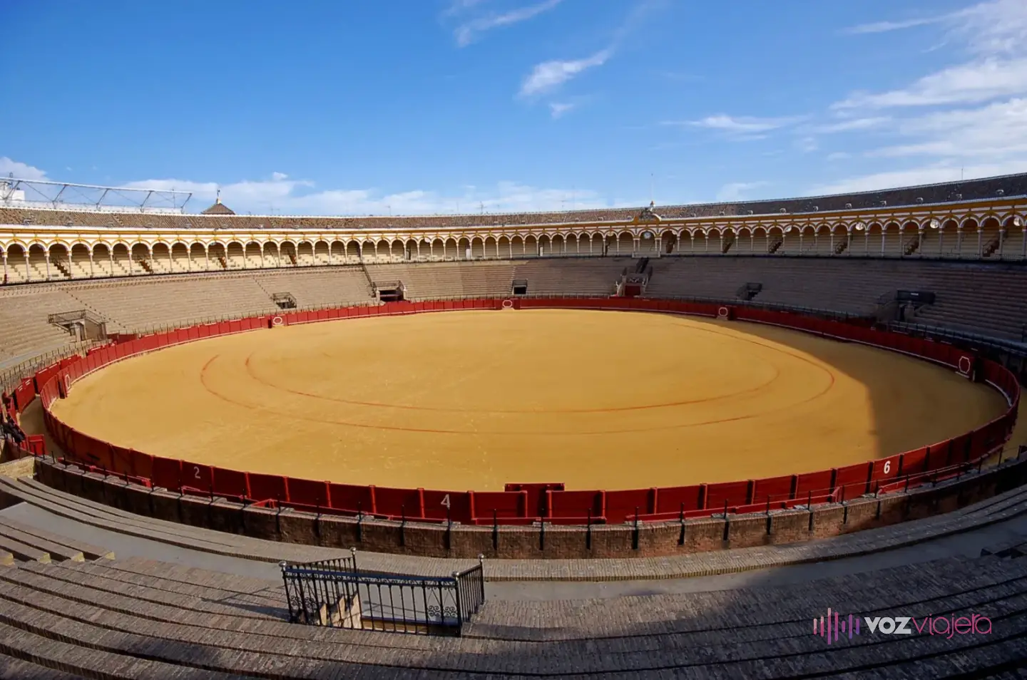 Ruedo de albero de la plaza de toros de la Maestranza de Sevilla, con la barrera roja, los tendidos de piedra y la arquería de la grada cubierta alrededor