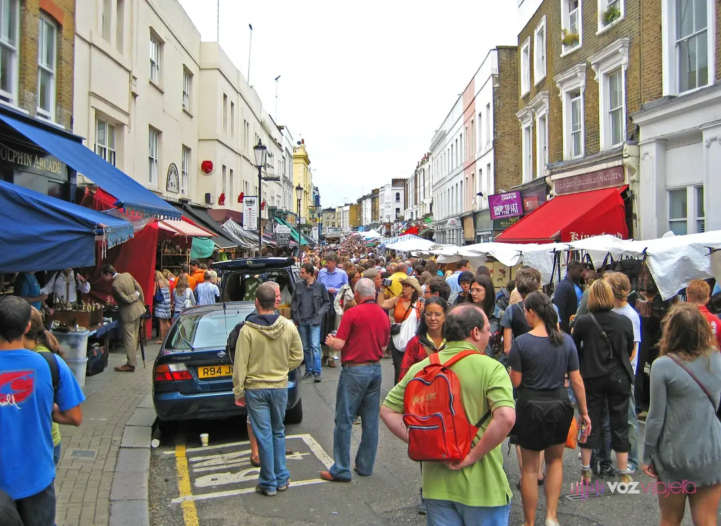 Portobello Road llena de gente un día de mercado, con toldos de tiendas y lonas blancas de los puestos a los dos lados