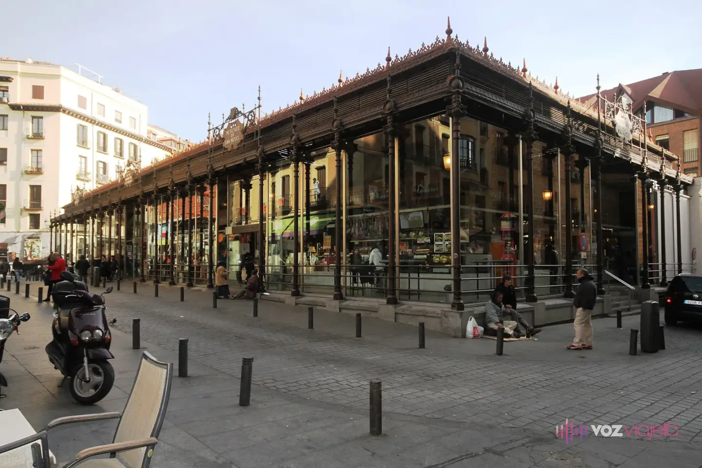 Edificio de hierro y cristal del Mercado de San Miguel en Madrid, con sus columnas de hierro oscuras, la crestería del tejado y la plaza adoquinada delante