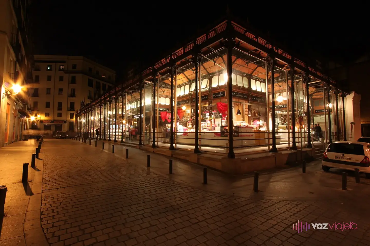El Mercado de San Miguel de noche, con el interior iluminado detrás de las cristaleras y la calle adoquinada casi vacía