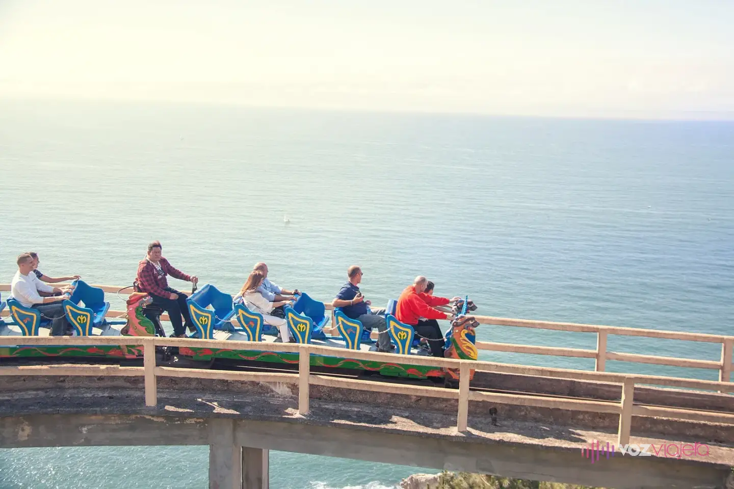 Vagonetas de la Montaña Suiza del Monte Igueldo con pasajeros sobre un tramo elevado con barandilla, con el mar Cantábrico detrás