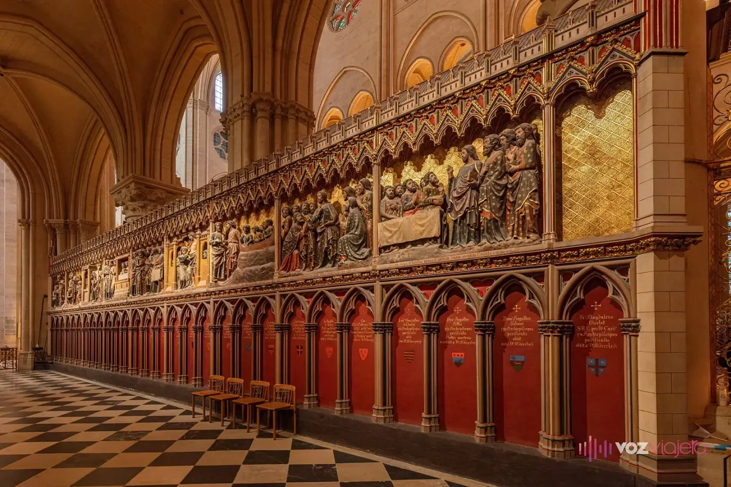 Relieves de piedra policromada del cerramiento del coro de Notre Dame, con escenas en arcos góticos sobre puertas rojas y suelo ajedrezado