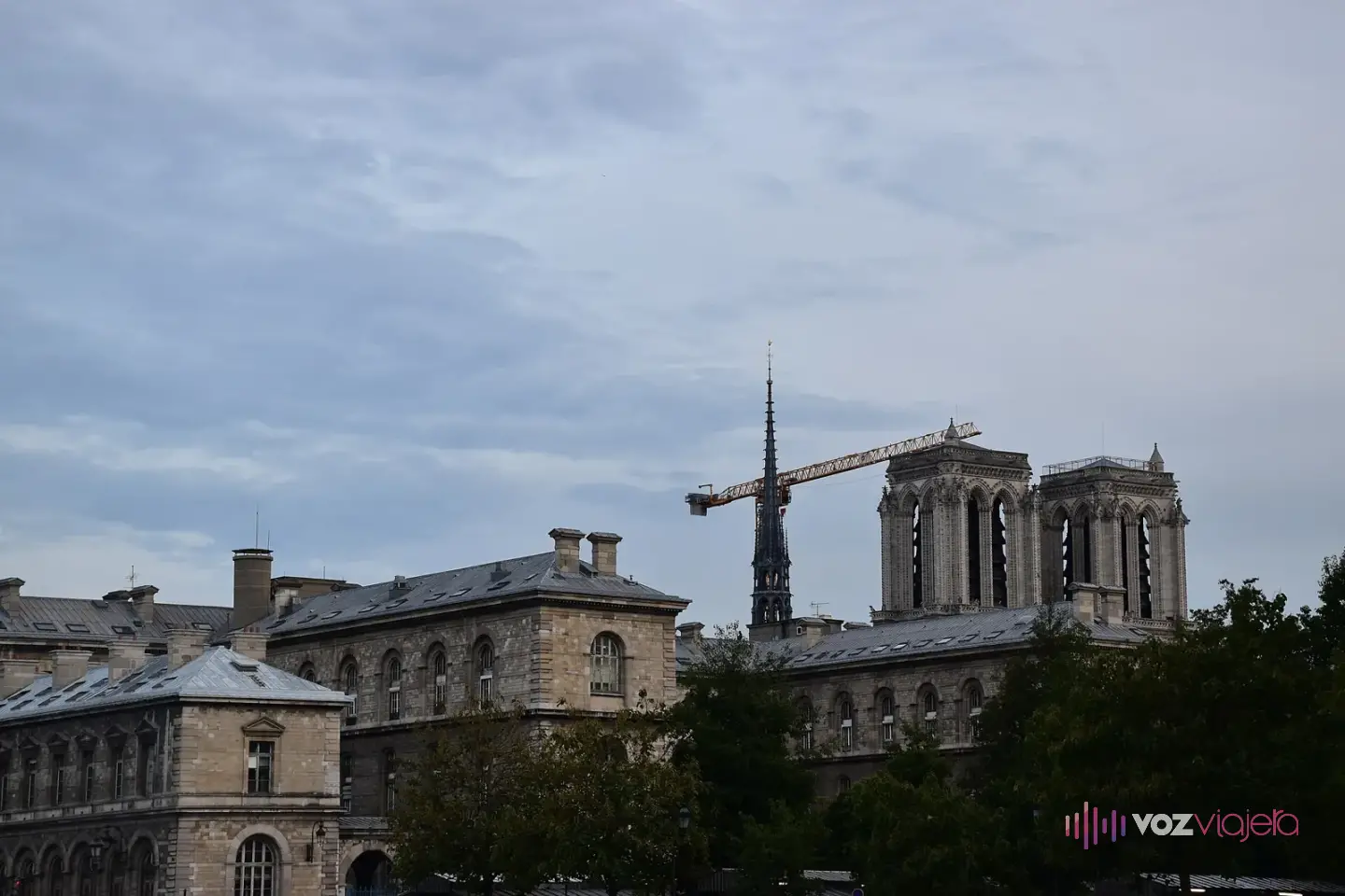 Las torres y la aguja de Notre Dame tras los tejados de la isla de la Cité, con una grúa de obra junto a la aguja, un día nublado