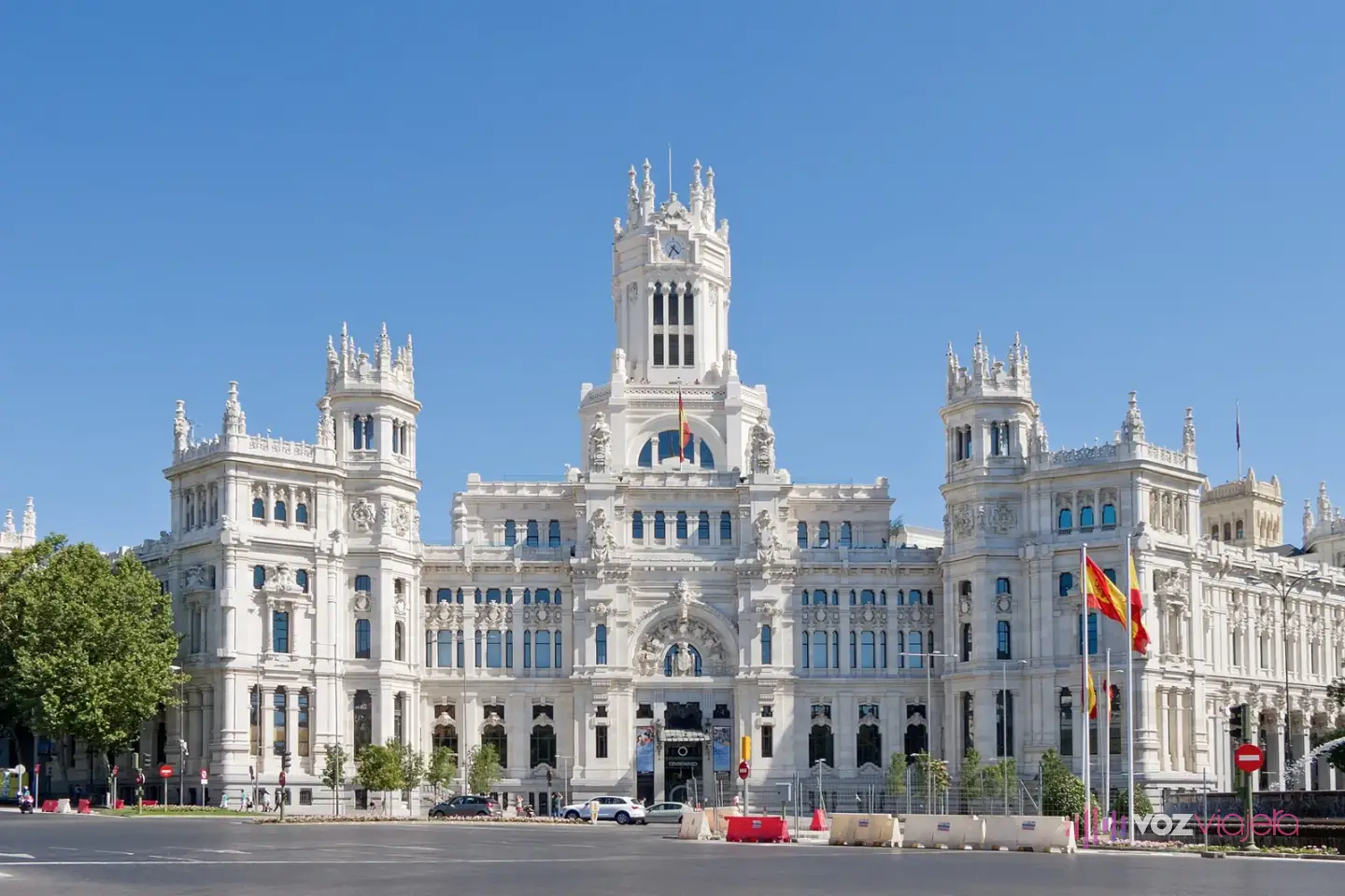 Fachada blanca del Palacio de Cibeles, con su torre central y 2 torres laterales con pináculos, visto desde la plaza en un día despejado