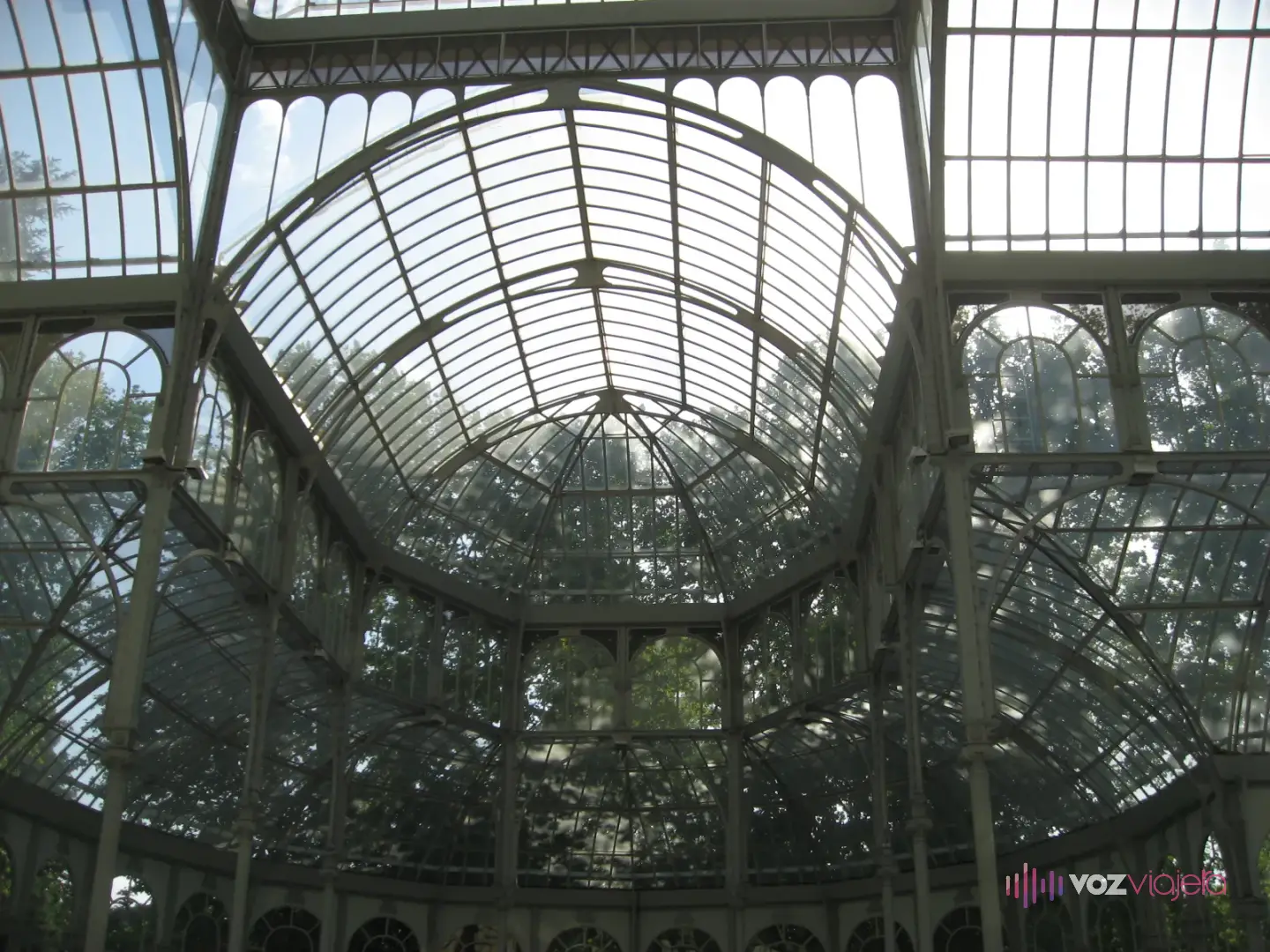 Interior del Palacio de Cristal mirando hacia arriba: la cúpula y las bóvedas de vidrio sostenidas por una estructura de hierro pintada de verde claro
