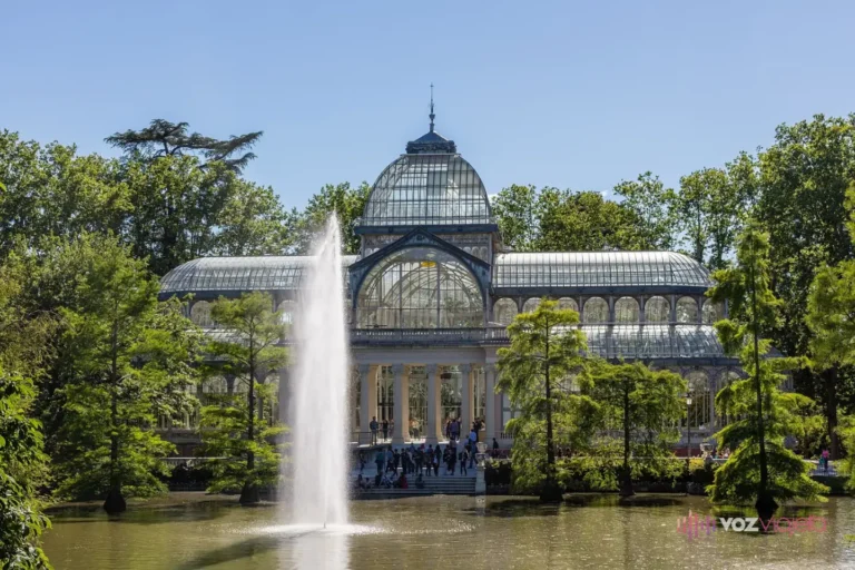 El Palacio de Cristal del Retiro de frente, con su cúpula de hierro y vidrio, el surtidor del lago delante y cipreses de los pantanos en el agua
