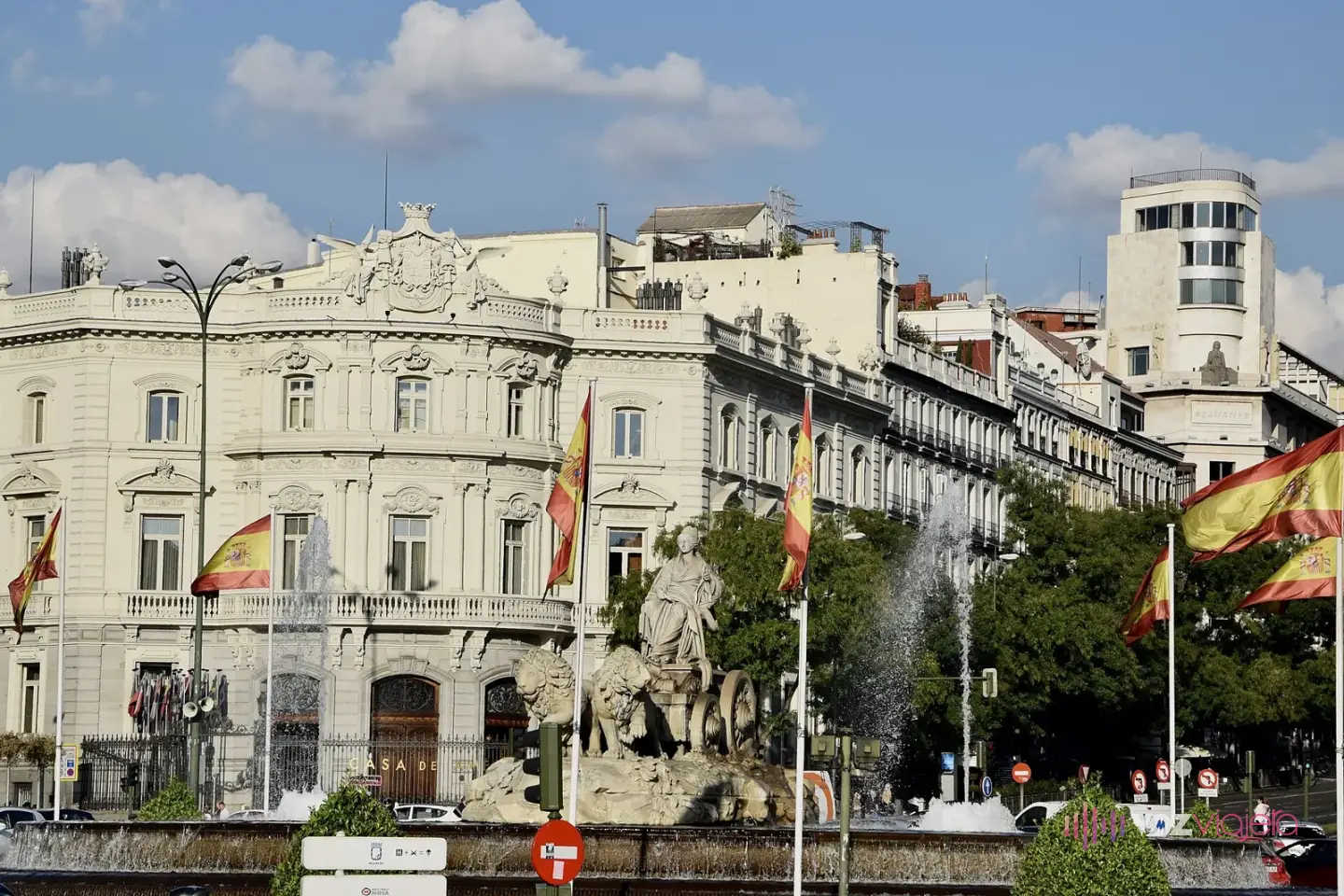 El Palacio de Linares, de fachada clara con balcones y banderas de España delante, con la Fuente de Cibeles y uno de sus surtidores en primer plano