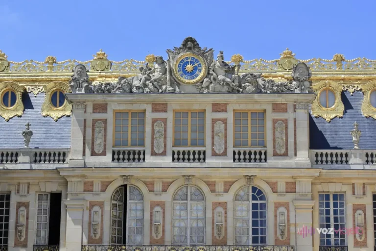 Fachada de ladrillo y piedra de la Cour de Marbre del Palacio de Versalles, con el gran reloj dorado y las esculturas sobre el tejado de pizarra