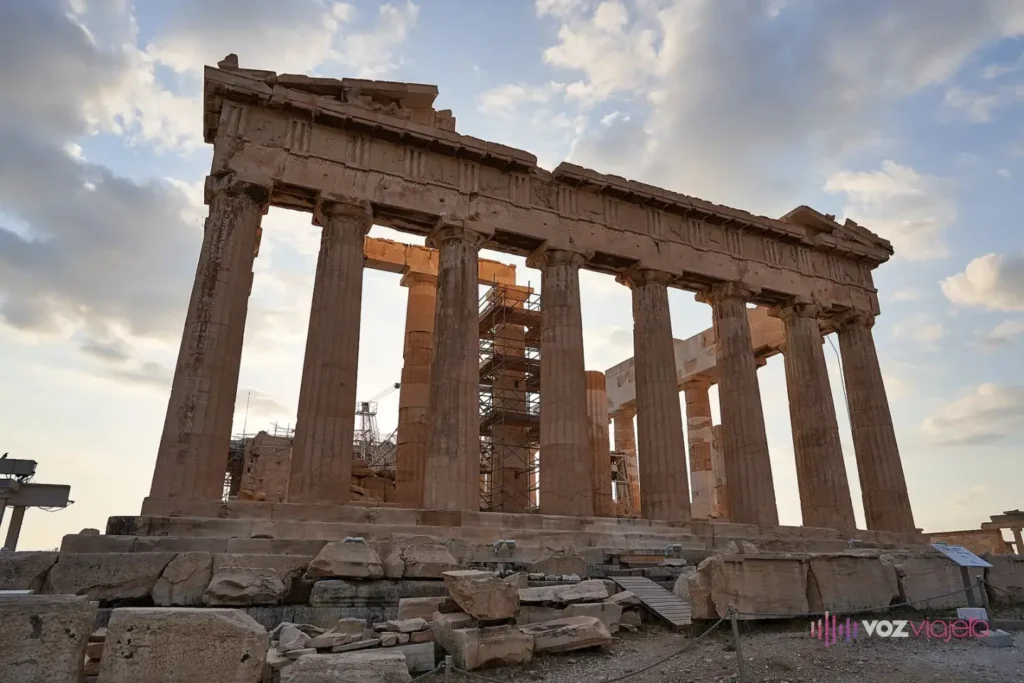 El Partenón visto desde abajo por su lado este: columnas dóricas desgastadas, bloques de mármol en el suelo en primer plano y una torre de andamio y una grúa dentro del templo