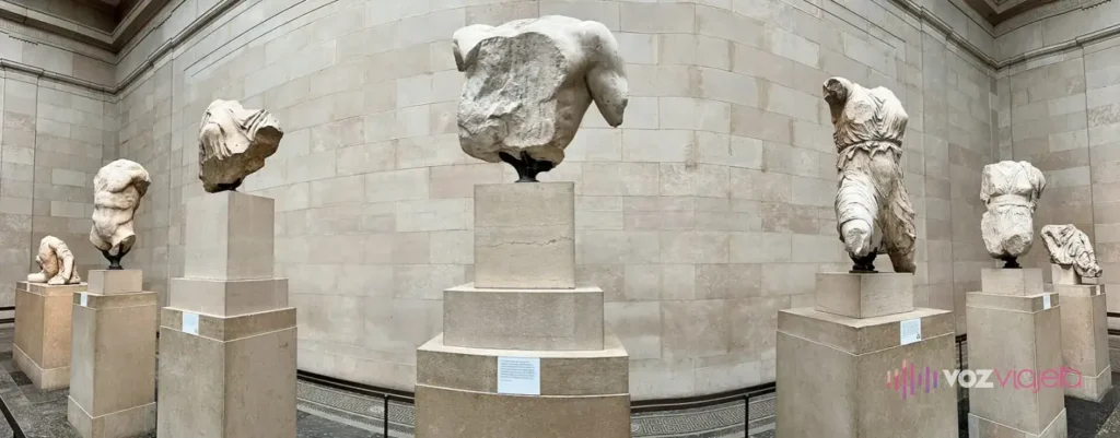 Figuras de mármol rotas del frontón oeste del Partenón sobre pedestales de piedra, a lo largo del muro curvo de una sala del Museo Británico: torsos masculinos y figuras femeninas con ropajes, sin cabeza