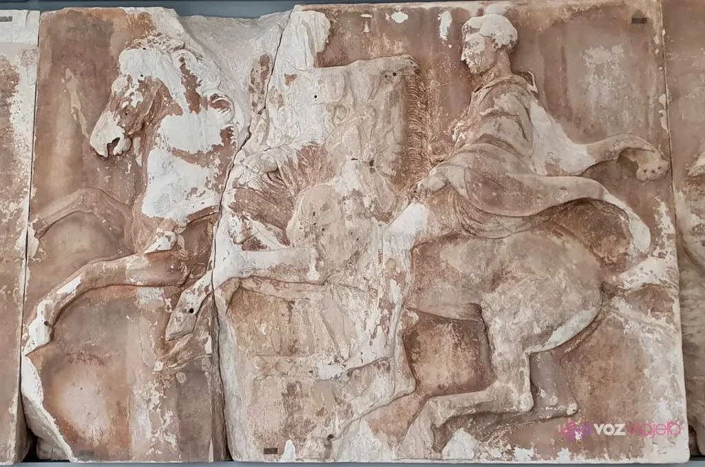 Una losa del friso oeste del Partenón: un jinete con manto sobre un caballo encabritado, en bajorrelieve sobre mármol desgastado con manchas anaranjadas