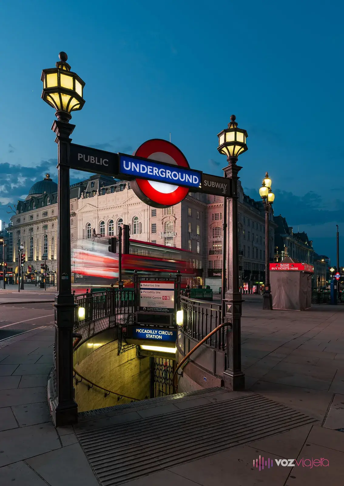 Boca de metro de Piccadilly Circus: una escalera que baja bajo el rótulo Underground, entre 2 farolas encendidas