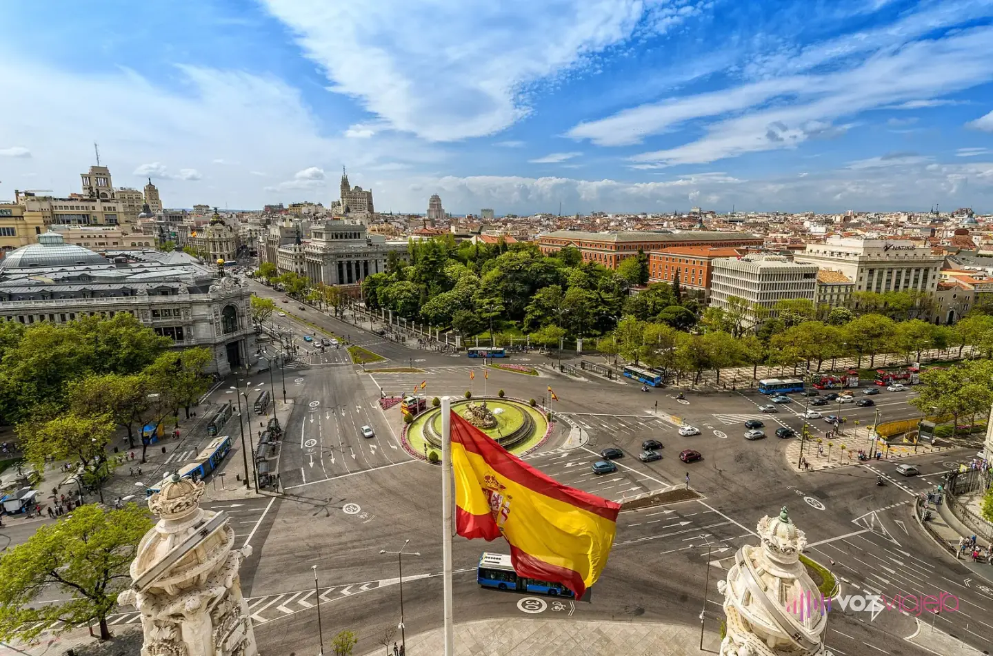 La Plaza de Cibeles vista desde lo alto del Palacio de Cibeles: la glorieta con la fuente en el centro, el tráfico alrededor, una bandera de España y los tejados de Madrid al fondo