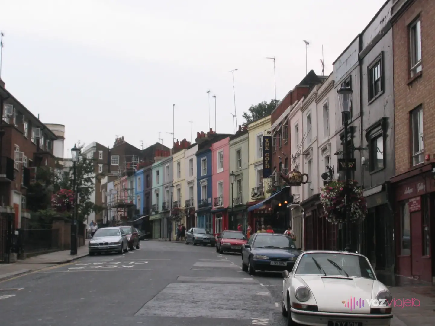 Portobello Road un día sin puestos, con casas pintadas de azul, rosa, verde y amarillo sobre las tiendas, cestas de flores en las farolas y coches aparcados