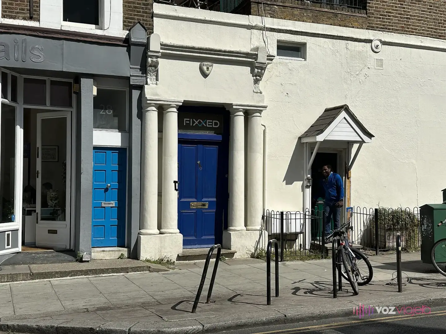 Fachada blanca con columnas y una puerta azul en Westbourne Park Road, junto a otra puerta azul más pequeña y un portabicicletas