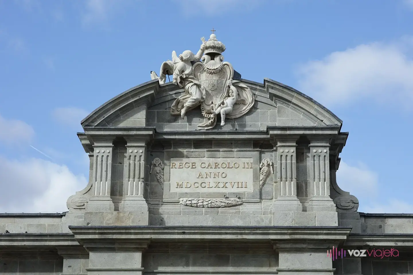 Ático de la Puerta de Alcalá con el escudo real sostenido por figuras esculpidas y, debajo, la lápida con la inscripción REGE CAROLO III ANNO MDCCLXXVIII