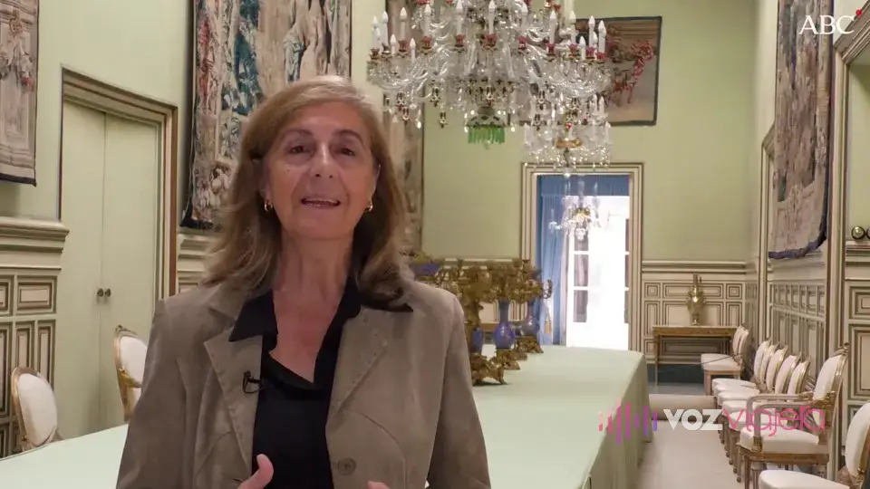 Fotograma de un vídeo de ABC de Sevilla en el Cuarto Real Alto del Real Alcázar: una mujer habla en un salón con lámpara de araña, tapices y una mesa de comedor