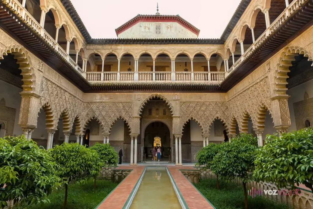 El Patio de las Doncellas del Real Alcázar de Sevilla: una alberca alargada en el centro entre 2 jardines hundidos de naranjos, rodeada de arcos mudéjares lobulados con yeserías y una galería alta