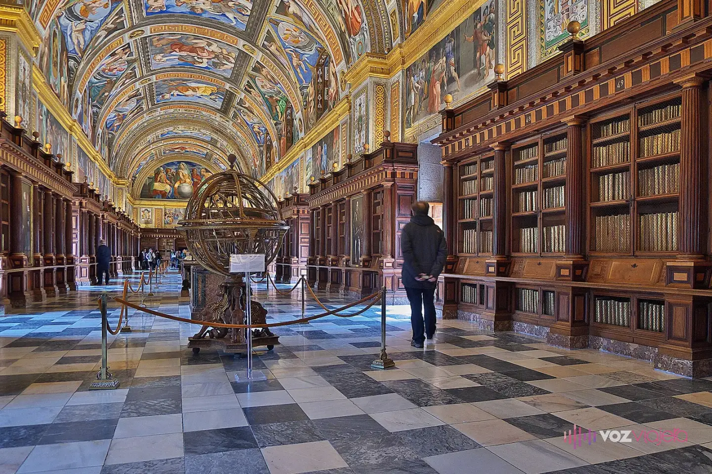Salón principal de la Real Biblioteca de El Escorial, con la bóveda de cañón cubierta de frescos, estanterías de madera noble y suelo de mármol