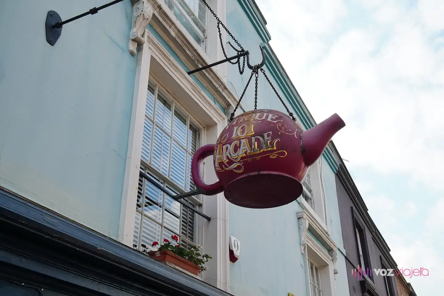 Una tetera roja gigante colgada como cartel sobre la fachada azul claro de una galería de antigüedades de Portobello Road