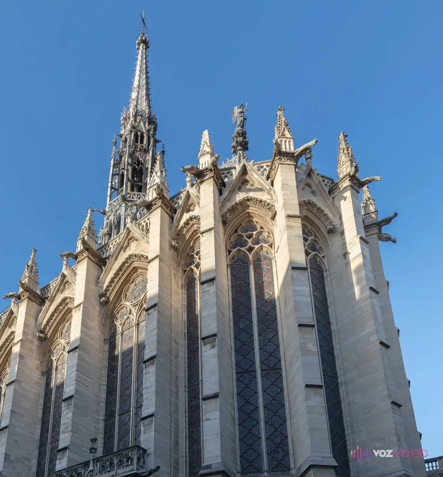 Exterior gótico de la Sainte-Chapelle visto desde abajo, con sus contrafuertes, gárgolas y la aguja contra el cielo azul