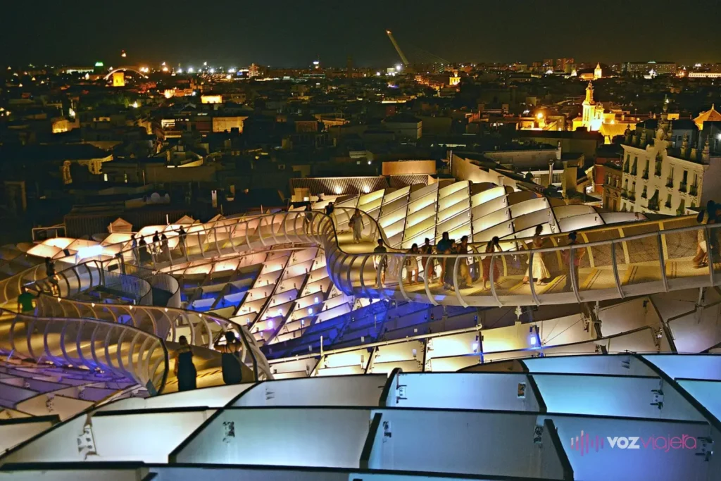 Las pasarelas de las Setas de Sevilla de noche, con la cubierta iluminada en tonos blancos y azulados y la ciudad encendida al fondo